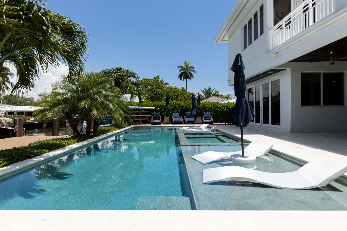 Modern backyard with swimming pool, artificial grass, stone path, trees, and chairs