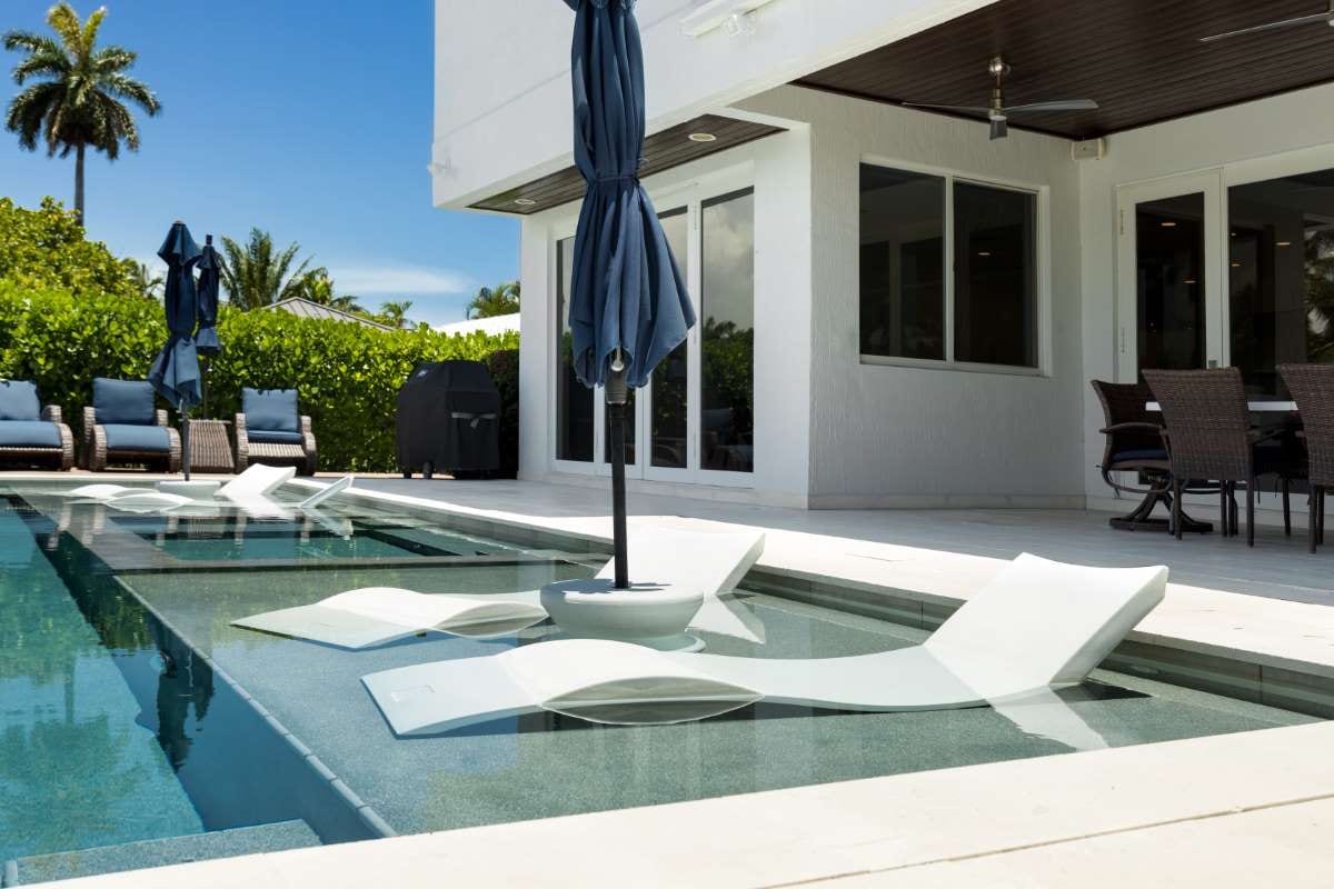 Modern backyard with swimming pool, artificial grass, stone path, trees and patio chairs