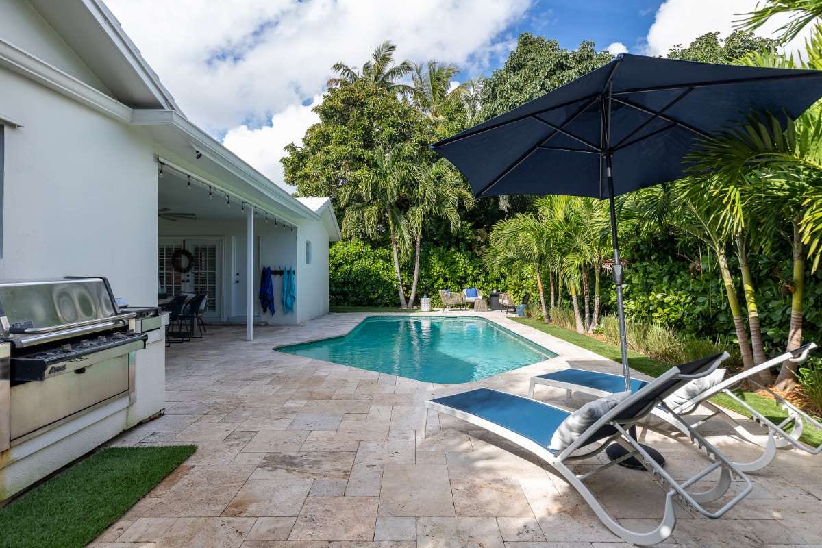 Modern backyard with pool, artificial grass, stone path, trees, and patio chairs