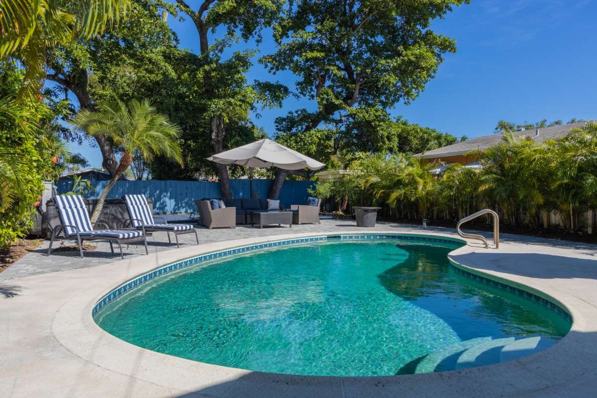 Modern backyard with swimming pool, artificial grass, stone path, trees, and patio chairs
