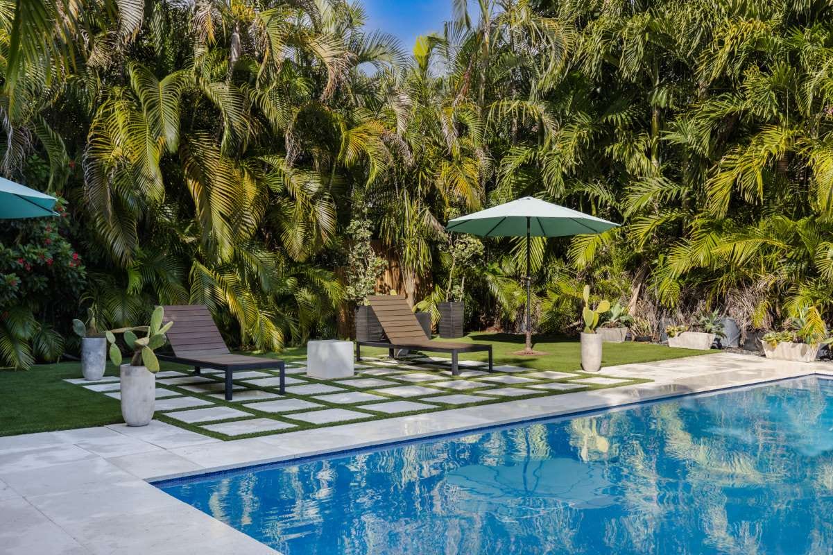 Modern backyard with pool, artificial grass, stone path, trees, and lounge chairs