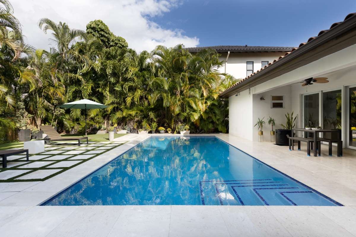 Backyard modern house with swimming pool, artificial grass, stone path, trees, and chairs