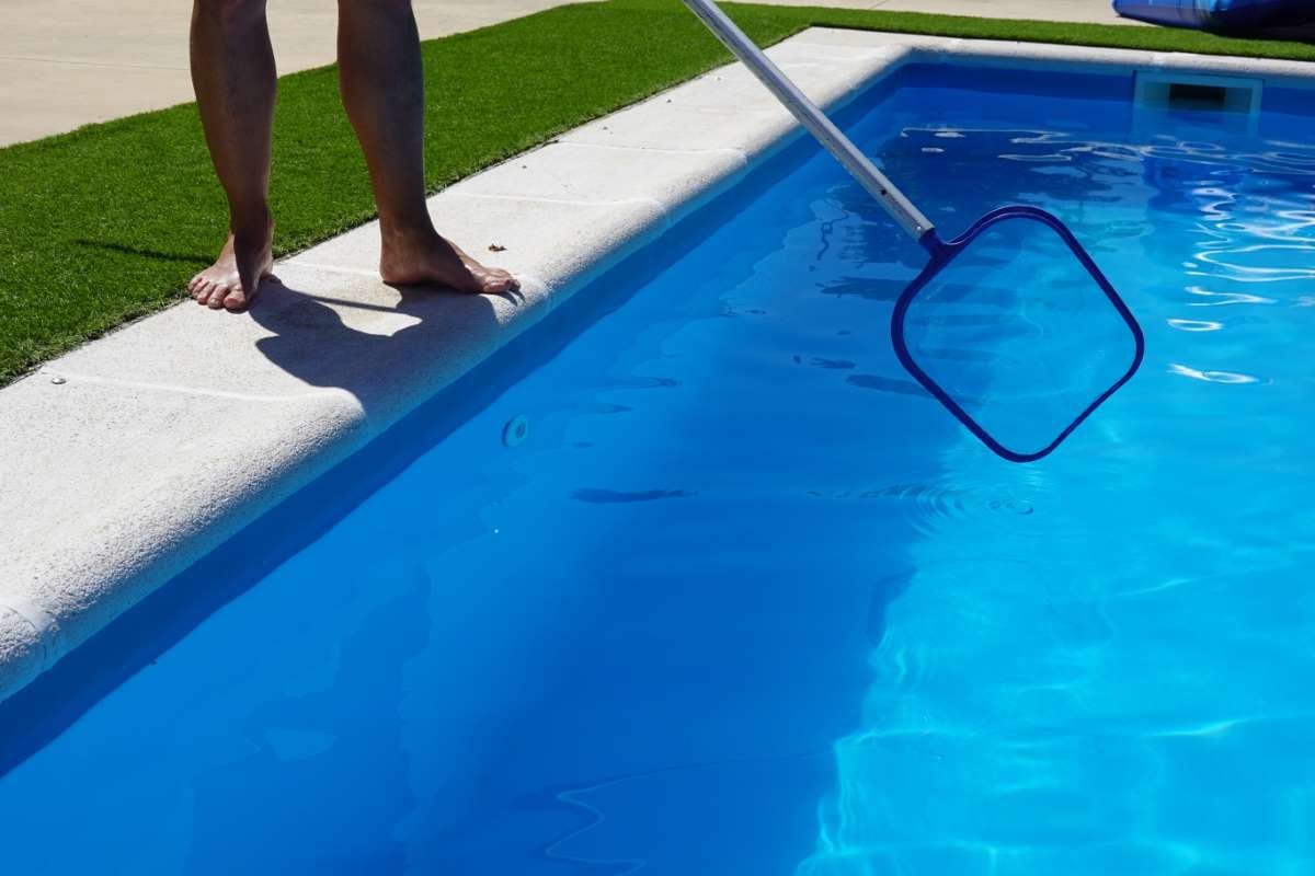 Man cleaning pool surface with a mesh skimmer