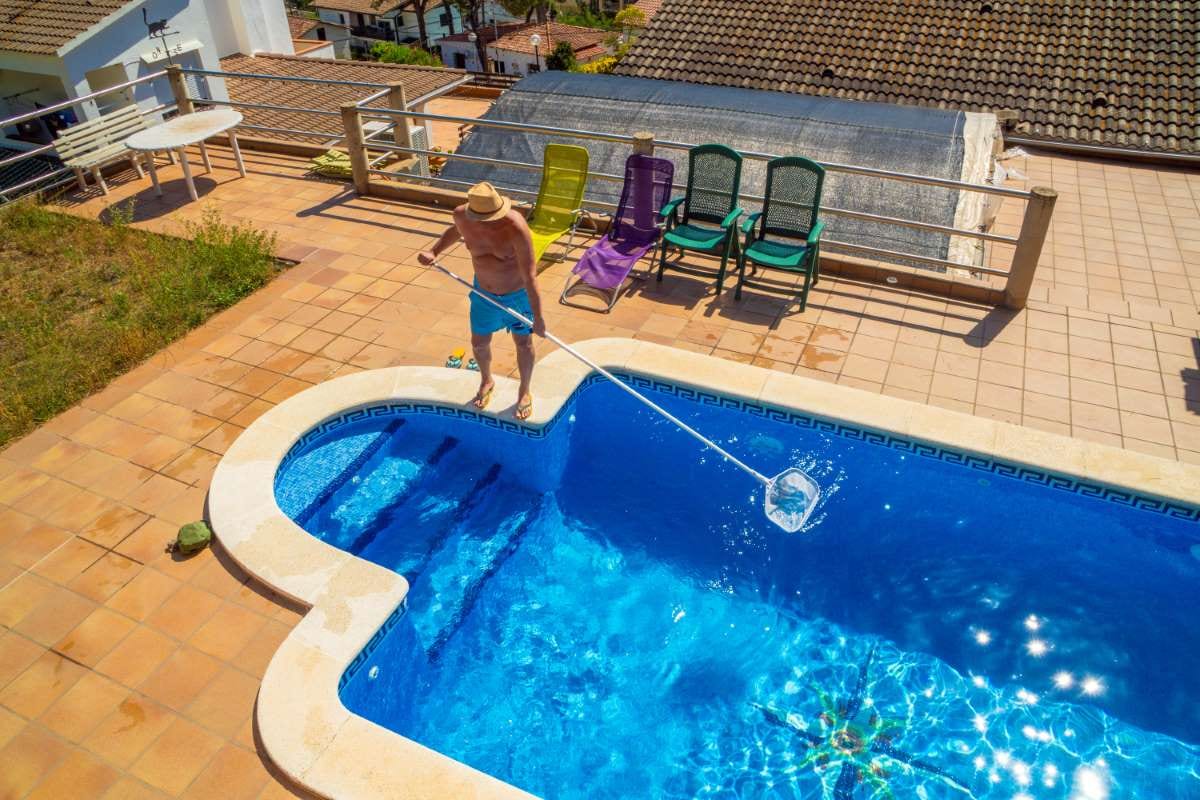 Man in straw hat cleaning a pool with a skimmer stick