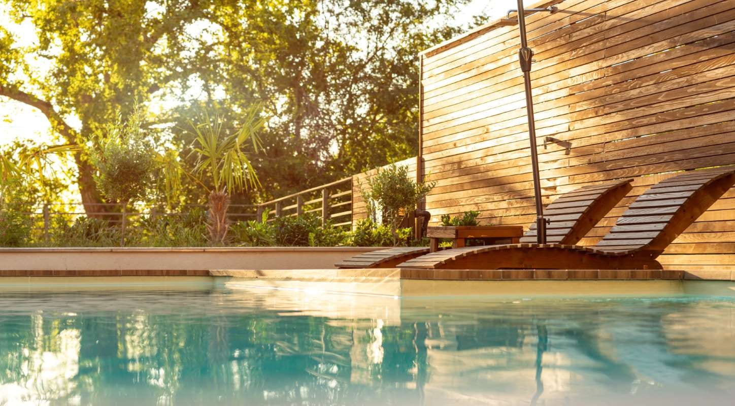 Luxury villa swimming pool at sunset with palm trees and wooden lounge chairs