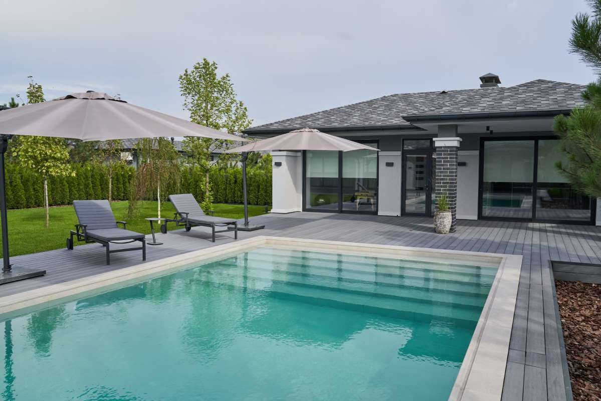 Modern residential pool terrace with umbrellas and chaise lounges beside a swimming pool